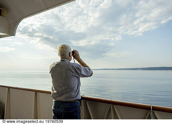 Senior man looking at sea through binoculars from ship
