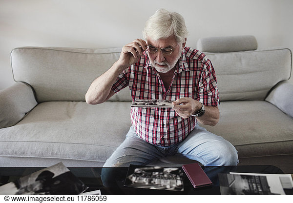 Senior man looking at vintage photographs while sitting on sofa at home
