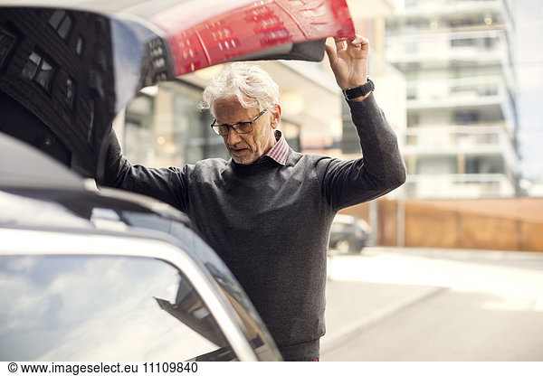 Senior man looking into car trunk while standing in city
