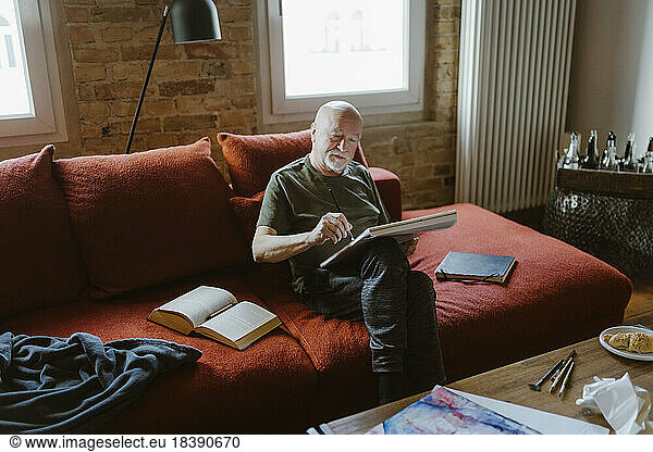 Senior man painting while sitting on sofa at home