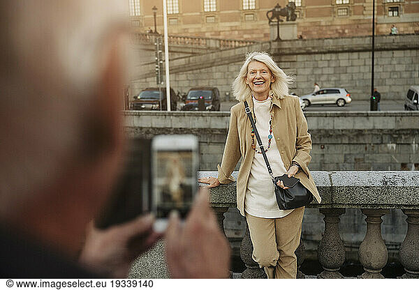 Senior man photographing happy woman leaning on railing
