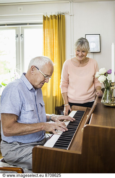 Senior man playing piano while woman looking at him indoors