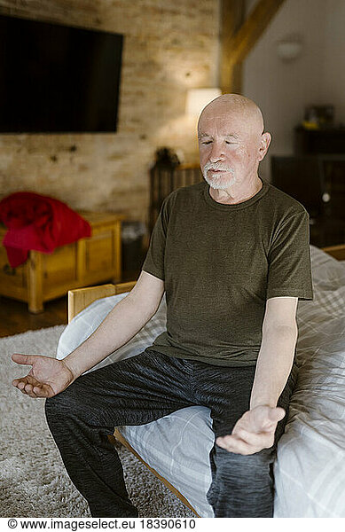 Senior man practicing yoga while sitting on bed at home