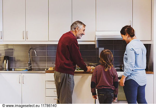 Senior man preparing food with great grandson and daughter in kitchen