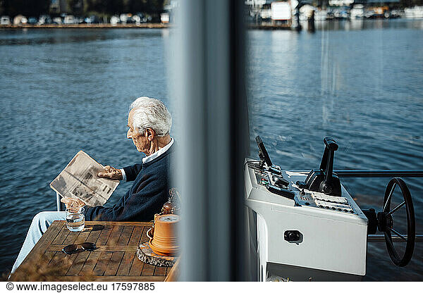 Senior man reading newspaper at houseboat on sunny day