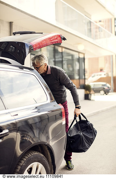 Senior man removing luggage from car trunk while standing in city
