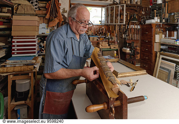 Senior man repairing fragile antique book spine in traditional bookbinding workshop
