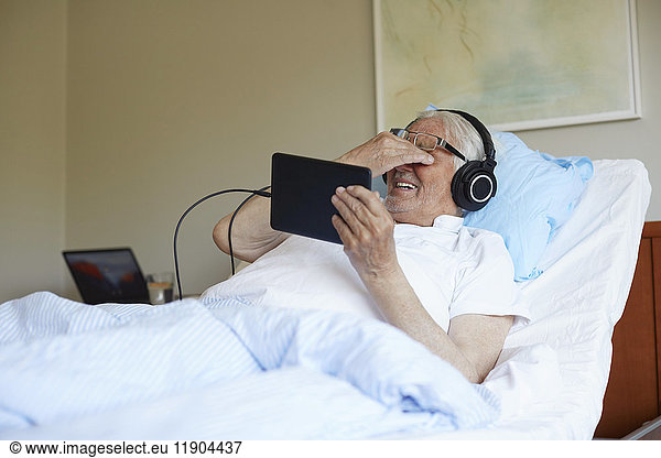 Senior man rubbing eyes while using digital tablet on bed in hospital ward
