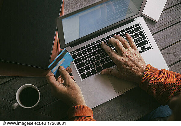 Senior man's hands doing online payment with credit card through laptop at home