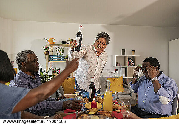 Senior man serving wine to friends sitting at dining table