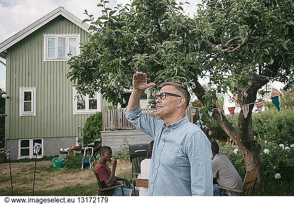 Senior man shielding eyes while standing in backyard during garden party
