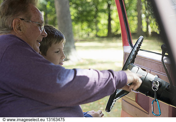 Senior man showing grandson pickup truck steering wheel