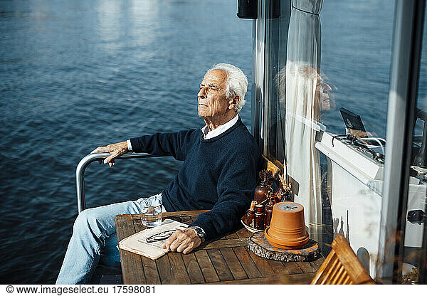 Senior man sitting by table at houseboat on sunny day