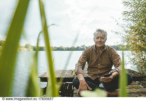 Senior man sitting cross-legged on jetty by lake