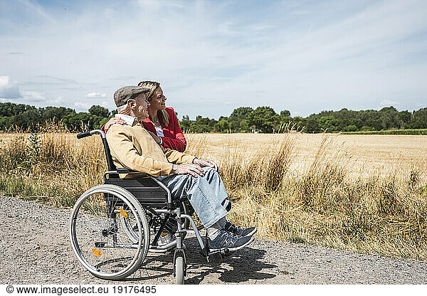 Senior man sitting in wheelchair by woman and looking at field