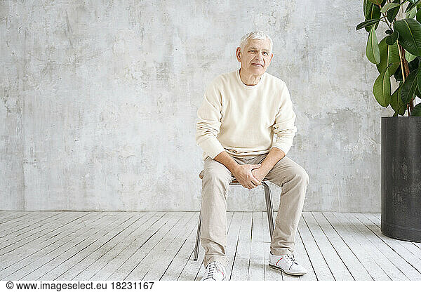 Senior man sitting on stool in front of wall