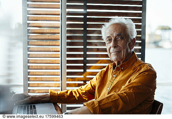 Senior man sitting with laptop at houseboat