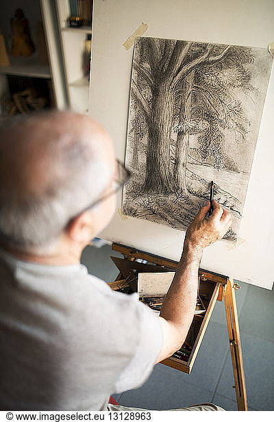 Senior man sketching on canvas at home