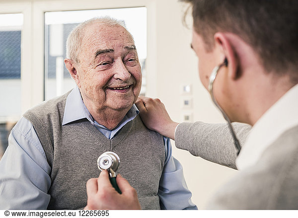 Senior man smiling at nurse with stethoscope at home