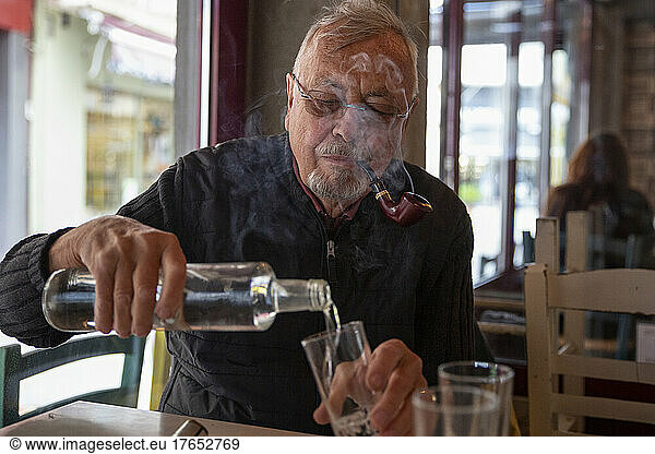 Senior man smoking cigar pouring drink in glass sitting at table