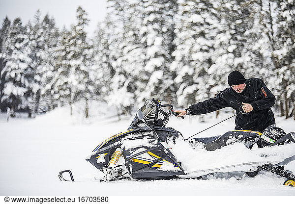 Senior man starting snowmobile with pull cord.