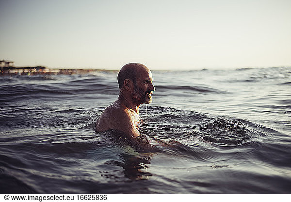 Senior man swimming in sea during sunset