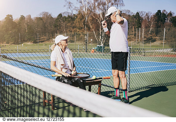 Senior man talking to friend at tennis court in summer