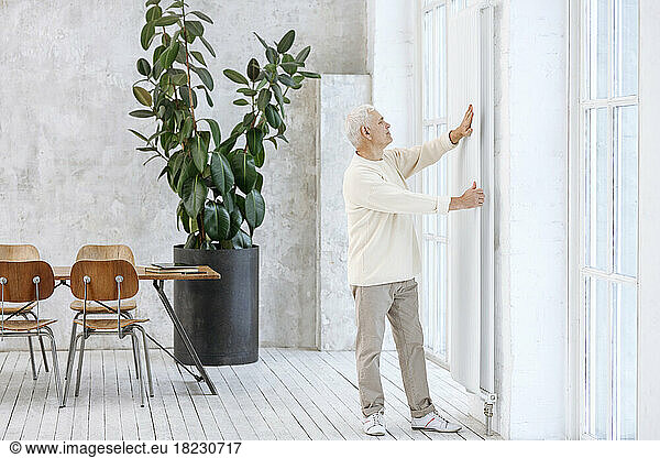 Senior man touching radiator standing at home