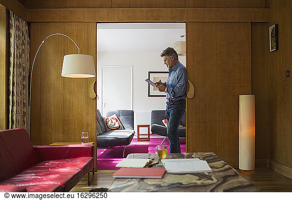 Senior man using digital tablet in living room doorway