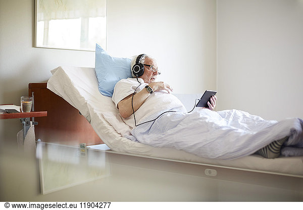 Senior man using digital tablet on bed in hospital ward