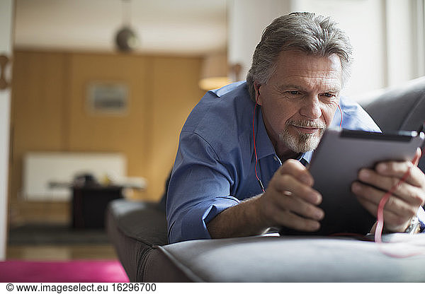 Senior man using headphones and digital tablet on living room sofa