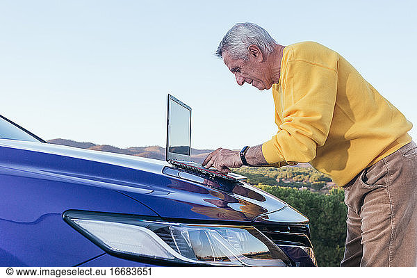 Senior man using laptop on car