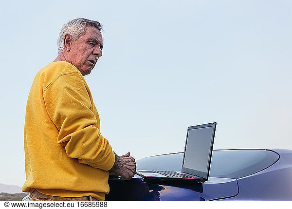 Senior man using laptop on car