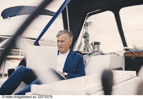 Senior man using laptop while sitting in yacht during vacation