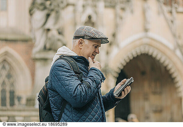 Senior man using smart phone standing in front of cathedral