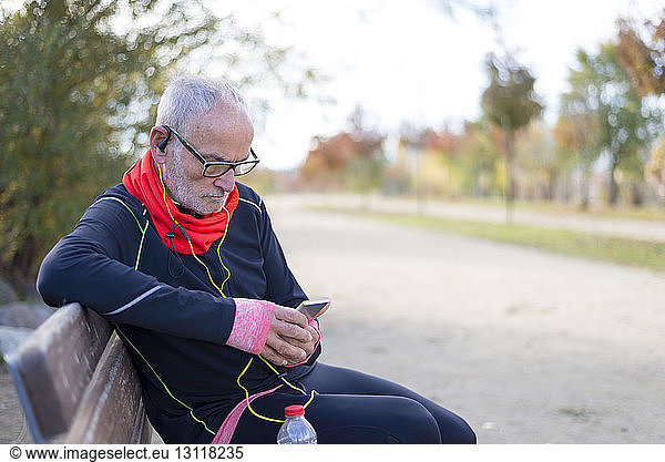 Senior man using smart phone while listening music on park bench