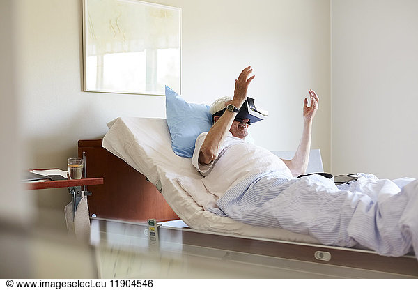 Senior man using VR glasses on bed in hospital ward