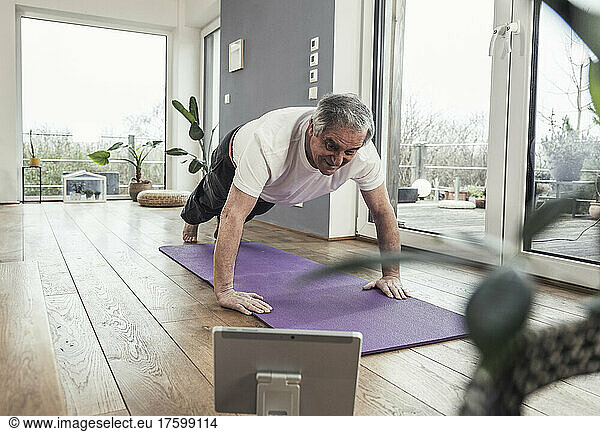 Senior man watching online tutorial doing push-ups at home