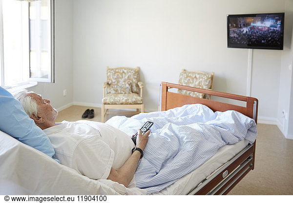 Senior man watching TV while reclining on bed in hospital ward