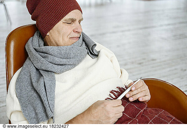 Senior man wearing warm clothing holding thermometer