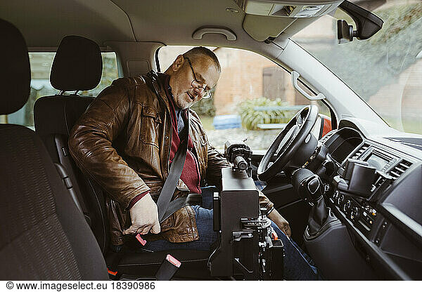 Senior man with disability fastening seat belt while sitting inside van