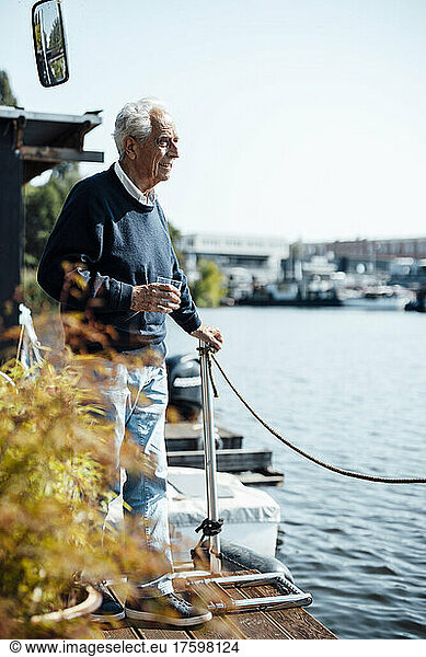 Senior man with drinking glass at houseboat on sunny day