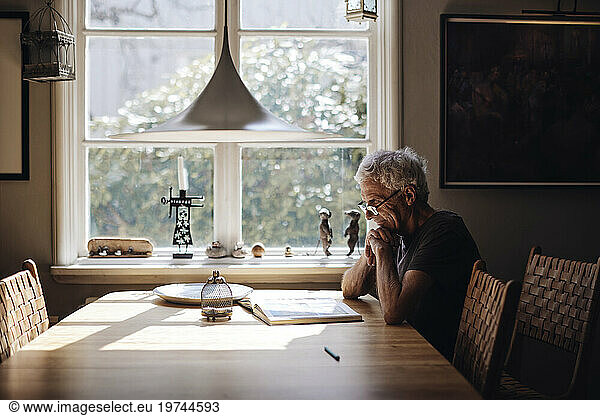 Senior man with eyeglasses reading book on table at home