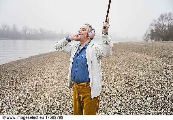 Senior man with eyes closed listening music through wireless headphones enjoying at beach