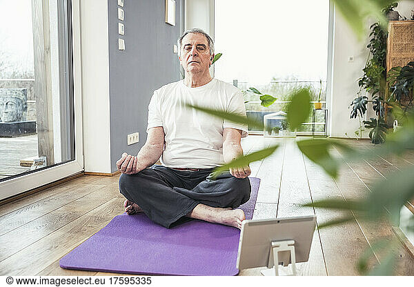 Senior man with eyes closed meditating on exercise mat at home