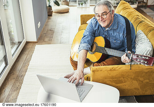 Senior man with guitar watching online tutorial on laptop in living room