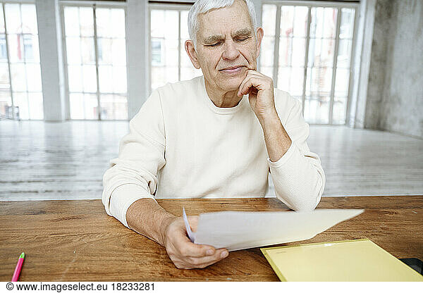 Senior man with hand on chin reading financial bills at home