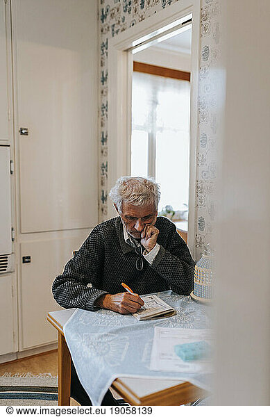 Senior man with hand on chin solving Soduko puzzle while sitting at home