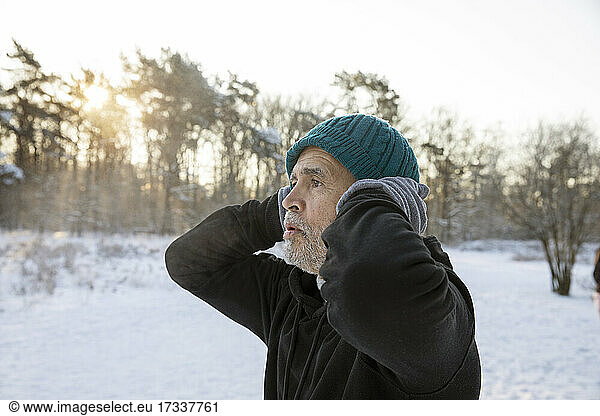 Senior man with hands behind head wearing knit hat during winter