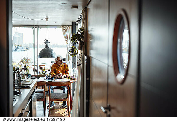Senior man with hands clasped sitting at table in houseboat
